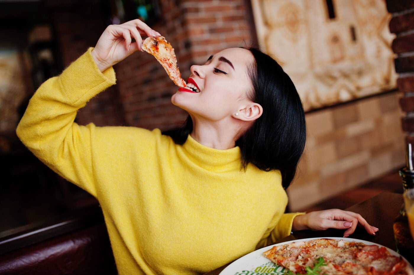 Funny,Brunette,Girl,In,Yellow,Sweater,Eating,Pizza,At,Restaurant.